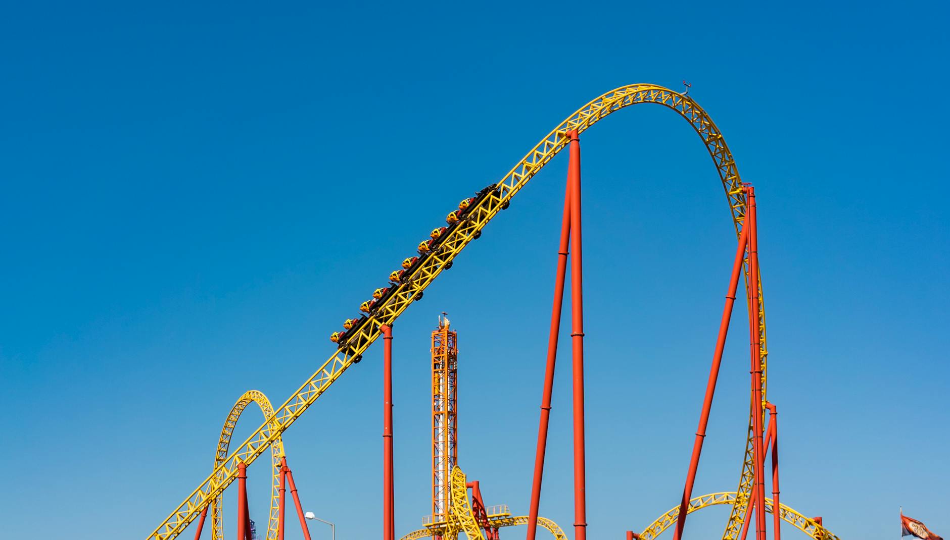 Riders on a steel roller coaster against blue sky at a theme park