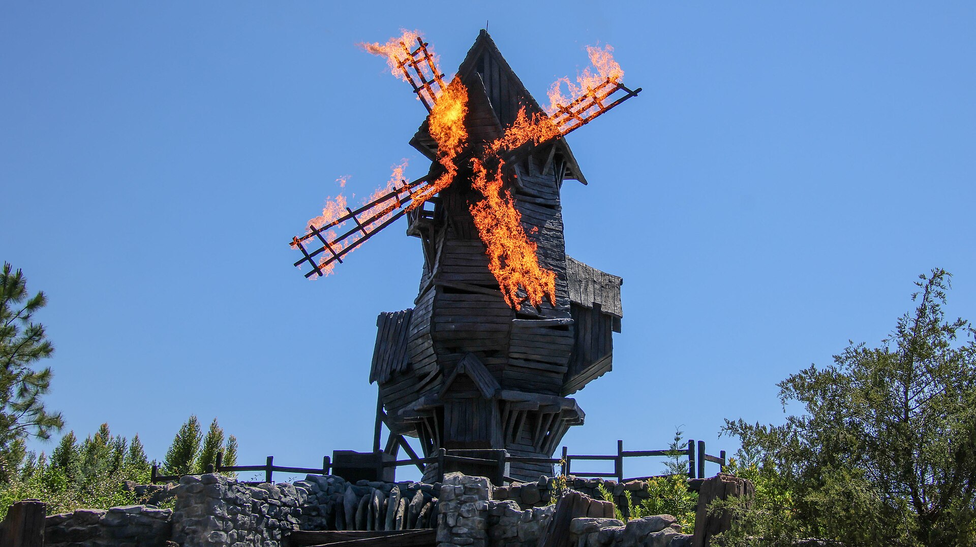 The wooden windmill on top of the Burning Blade Tavern with its sails engulfed in flames against a blue sky