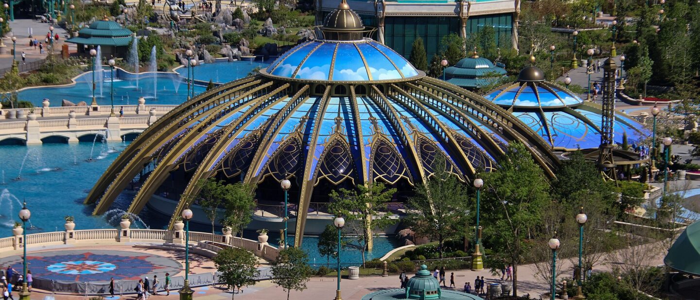 The blue and gold glass domes of the Constellation Carousel beside the fountains of Celestial Park at Epic Universe