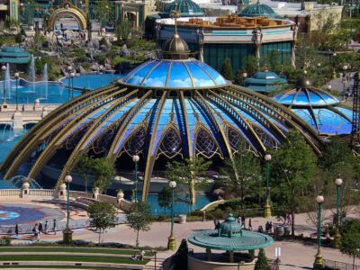 The blue and gold glass domes of the Constellation Carousel beside the fountains of Celestial Park at Epic Universe
