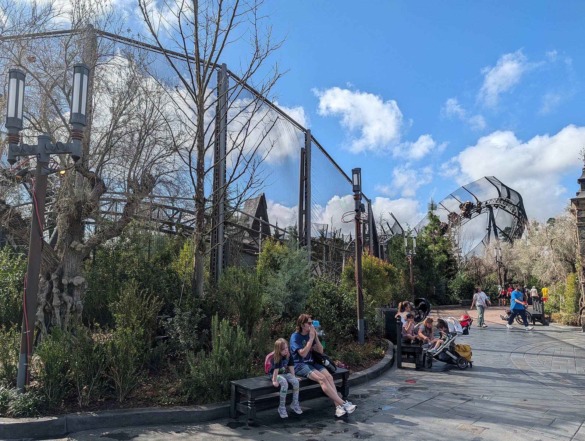 Curse of the Werewolf spinning coaster track and cars visible above netting and bare trees at the edge of Darkmoor, with visitors resting on a bench