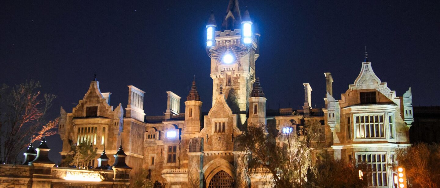 Frankenstein Manor lit up at night in Dark Universe, with glowing lights on its central tower and the Darkmoor village arch in the foreground