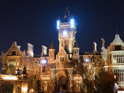 Frankenstein Manor lit up at night in Dark Universe, with glowing lights on its central tower and the Darkmoor village arch in the foreground