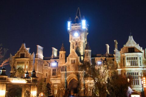 Frankenstein Manor lit up at night in Dark Universe, with glowing lights on its central tower and the Darkmoor village arch in the foreground