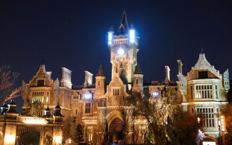 Frankenstein Manor lit up at night in Dark Universe, with glowing lights on its central tower and the Darkmoor village arch in the foreground