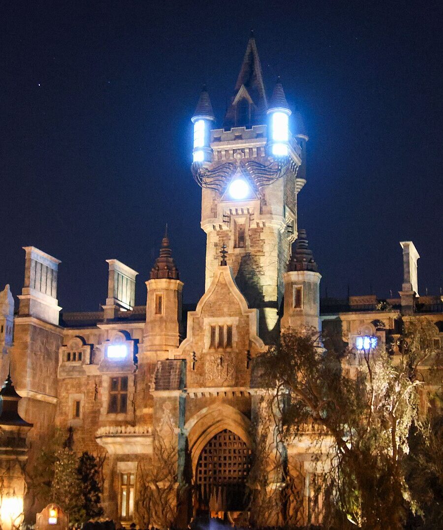 Frankenstein Manor lit up at night in Dark Universe, with glowing lights on its central tower and the Darkmoor village arch in the foreground