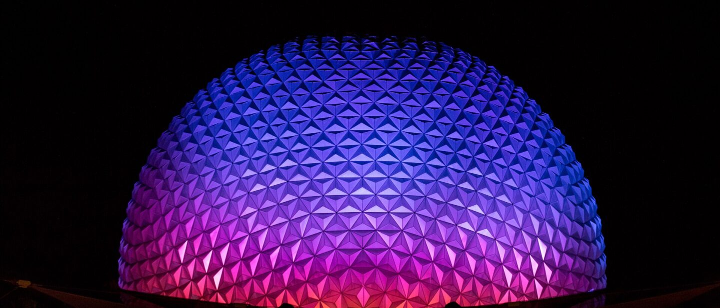 Spaceship Earth at EPCOT lit in purple, blue and pink against a black night sky