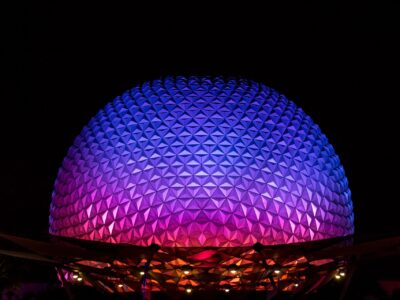 Spaceship Earth at EPCOT lit in purple, blue and pink against a black night sky