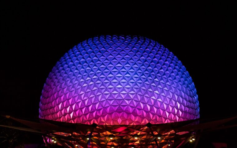 Spaceship Earth at EPCOT lit in purple, blue and pink against a black night sky