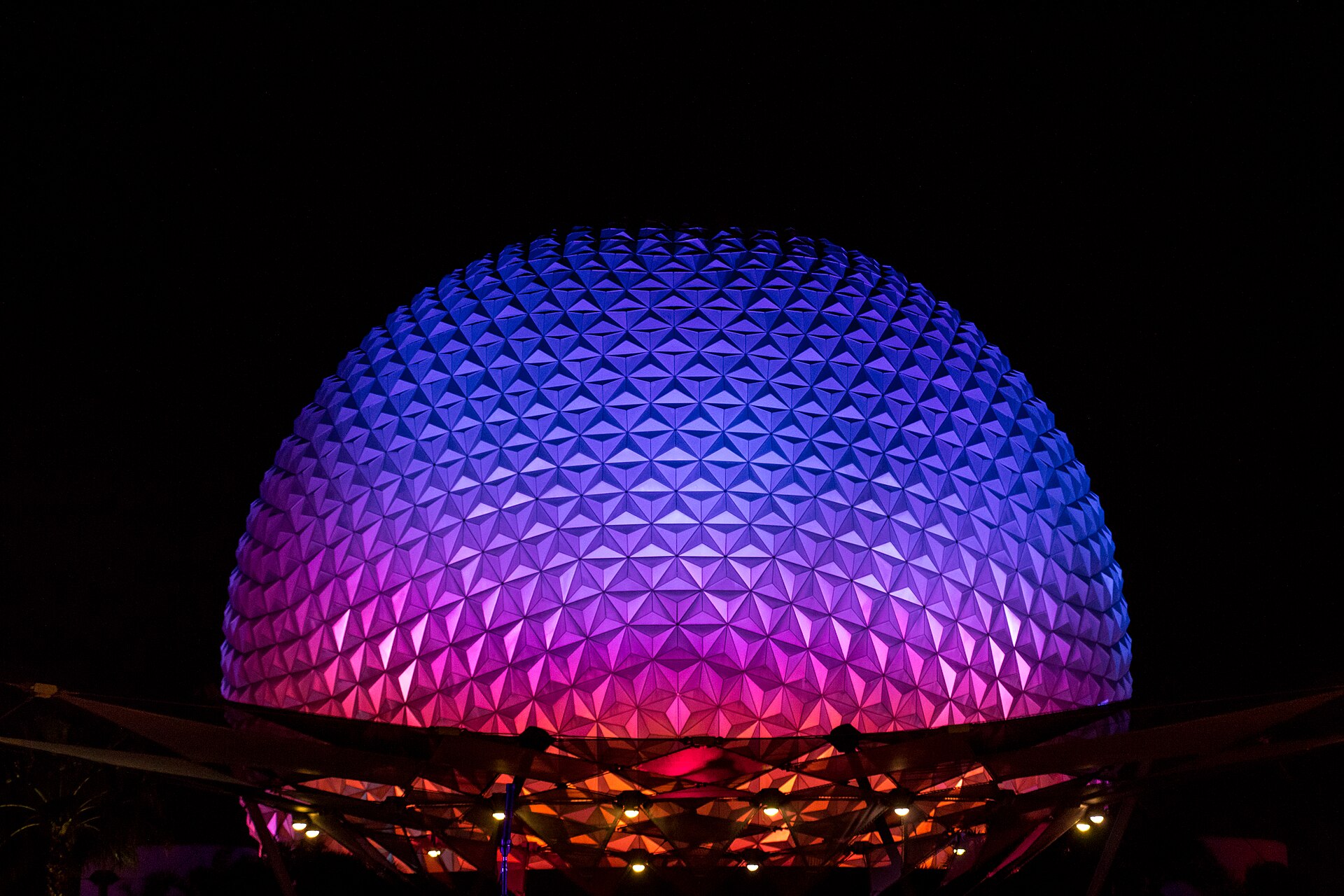 Spaceship Earth at EPCOT lit in purple, blue and pink against a black night sky