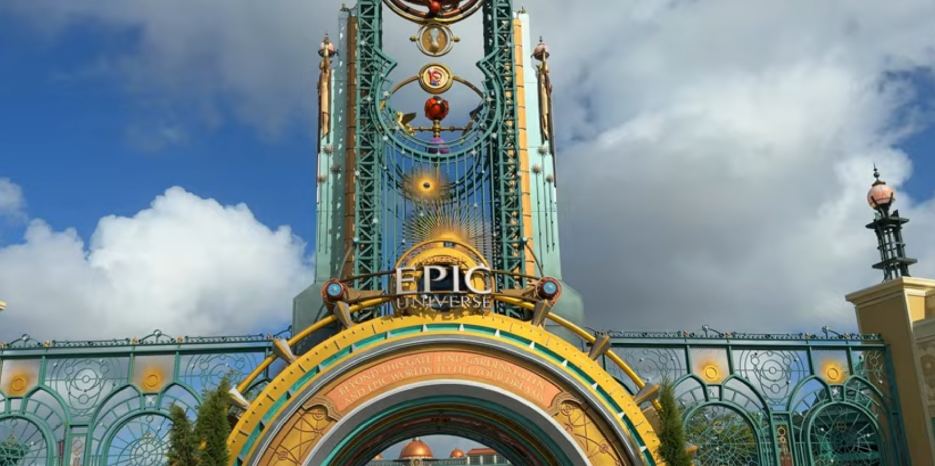 The ornate green and gold Epic Universe entrance gate, with the copper domes of the Helios Grand hotel visible through the arch