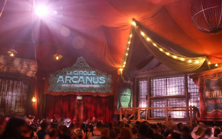 The red pre-show tent for Le Cirque Arcanus in the Ministry of Magic, with a painted sign, strings of lights and an audience waiting