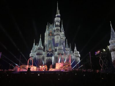 Cinderella Castle covered in lights at night with a stage show in front during a Magic Kingdom Christmas party