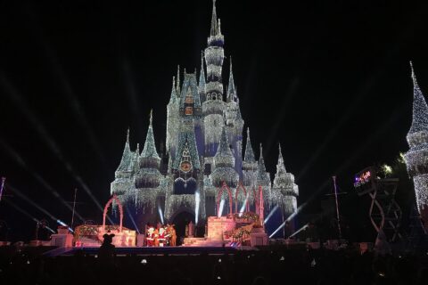 Cinderella Castle covered in lights at night with a stage show in front during a Magic Kingdom Christmas party