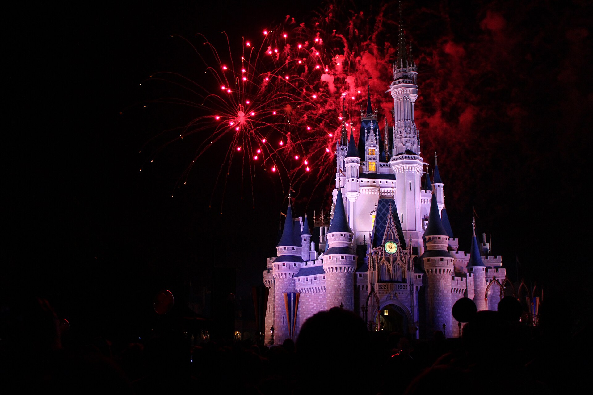 Cinderella Castle lit in pink and white at night with red fireworks bursting above it