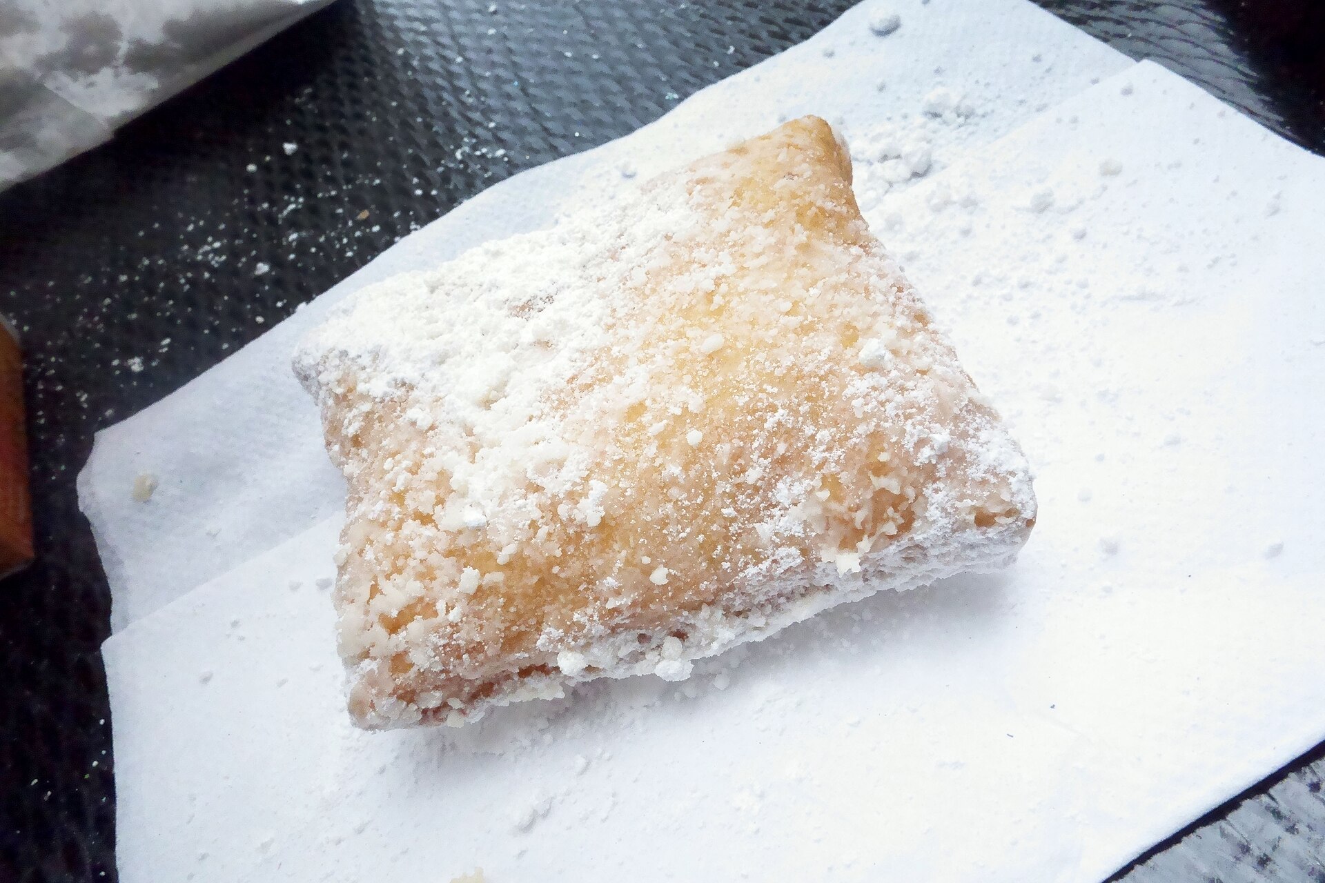 A single square beignet covered in powdered sugar on a paper napkin