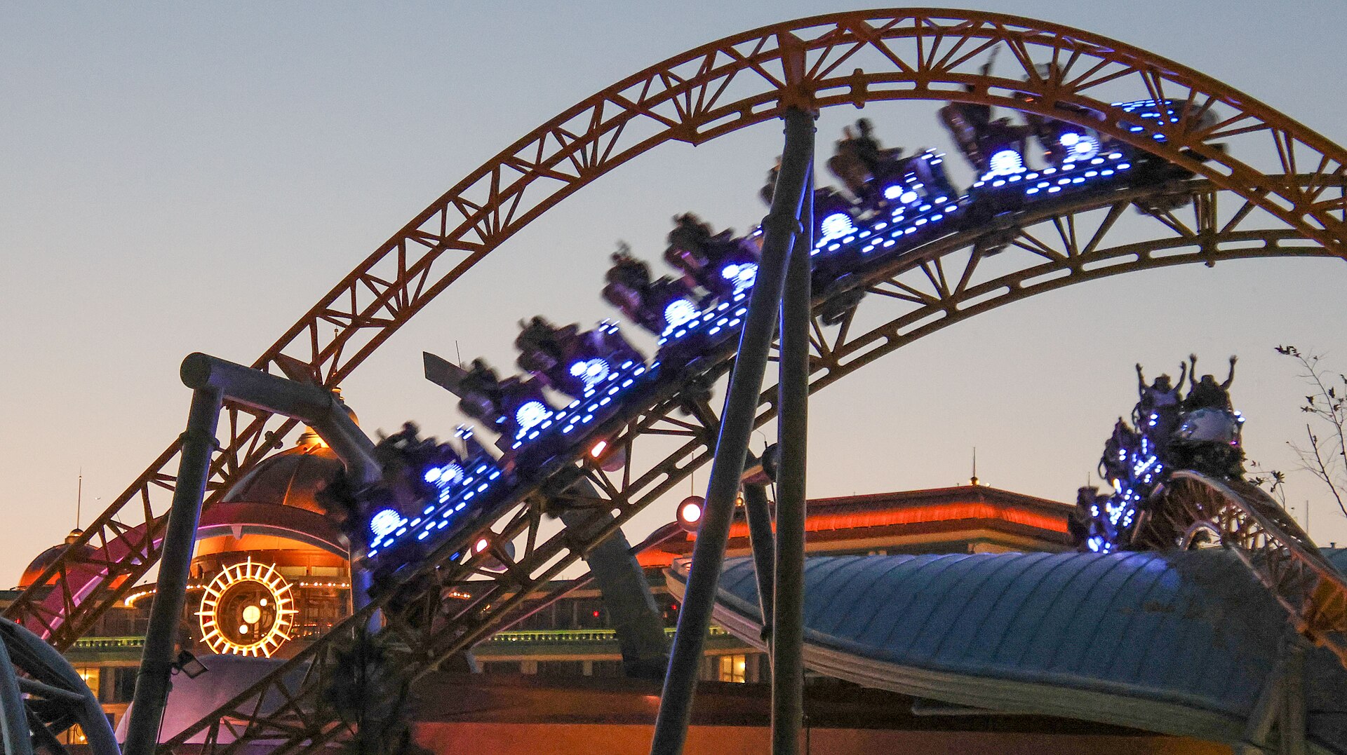 Stardust Racers coaster trains lit with blue lights racing over an orange steel track at twilight in Celestial Park at Epic Universe