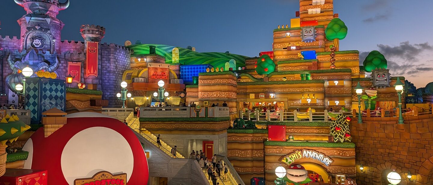 Super Nintendo World at Epic Universe at dusk, with the red mushroom Toadstool Cafe in the foreground and Bowser's castle and Yoshi's Adventure behind
