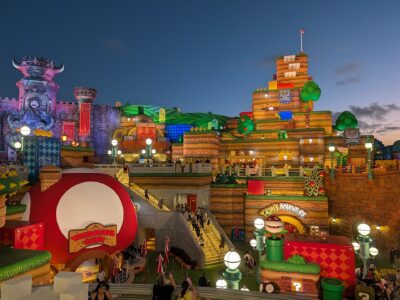 Super Nintendo World at Epic Universe at dusk, with the red mushroom Toadstool Cafe in the foreground and Bowser's castle and Yoshi's Adventure behind