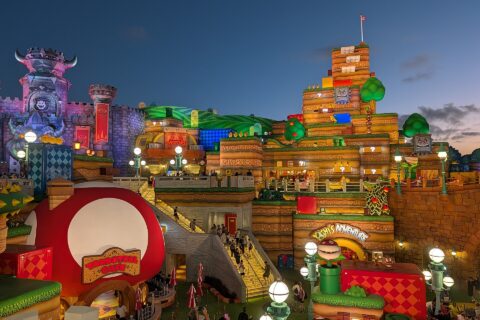 Super Nintendo World at Epic Universe at dusk, with the red mushroom Toadstool Cafe in the foreground and Bowser's castle and Yoshi's Adventure behind