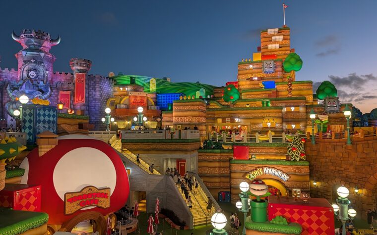 Super Nintendo World at Epic Universe at dusk, with the red mushroom Toadstool Cafe in the foreground and Bowser's castle and Yoshi's Adventure behind