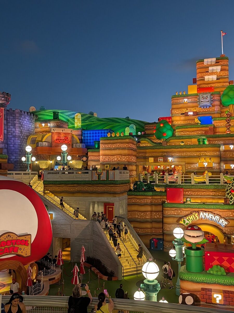 Super Nintendo World at Epic Universe at dusk, with the red mushroom Toadstool Cafe in the foreground and Bowser's castle and Yoshi's Adventure behind