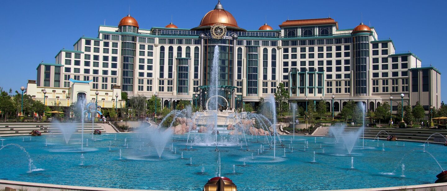 Universal Helios Grand Hotel, a large cream building with copper domes, seen across the dancing fountains of Celestial Park