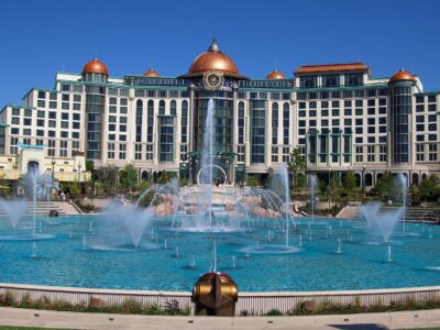 Universal Helios Grand Hotel, a large cream building with copper domes, seen across the dancing fountains of Celestial Park