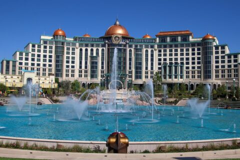 Universal Helios Grand Hotel, a large cream building with copper domes, seen across the dancing fountains of Celestial Park