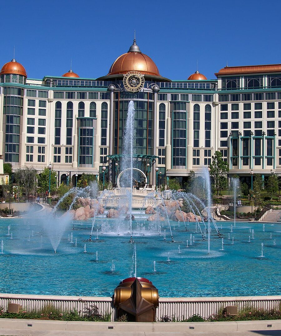 Universal Helios Grand Hotel, a large cream building with copper domes, seen across the dancing fountains of Celestial Park
