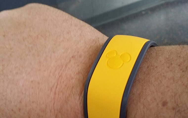 A yellow Disney MagicBand with an embossed Mickey Mouse head worn on a wrist