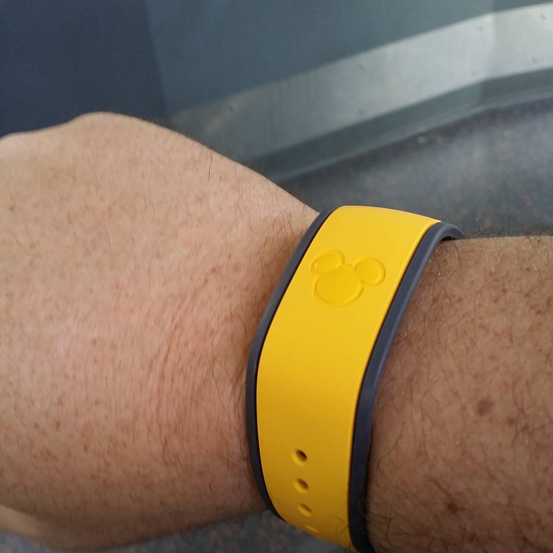 A yellow Disney MagicBand with an embossed Mickey Mouse head worn on a wrist