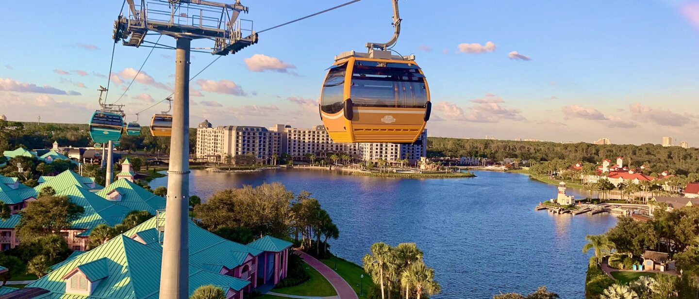 Disney Skyliner gondolas travelling on their cable above Disney's Caribbean Beach Resort, with a lake and resort buildings below