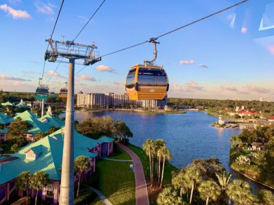 Disney Skyliner gondolas travelling on their cable above Disney's Caribbean Beach Resort, with a lake and resort buildings below