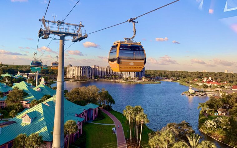 Disney Skyliner gondolas travelling on their cable above Disney's Caribbean Beach Resort, with a lake and resort buildings below