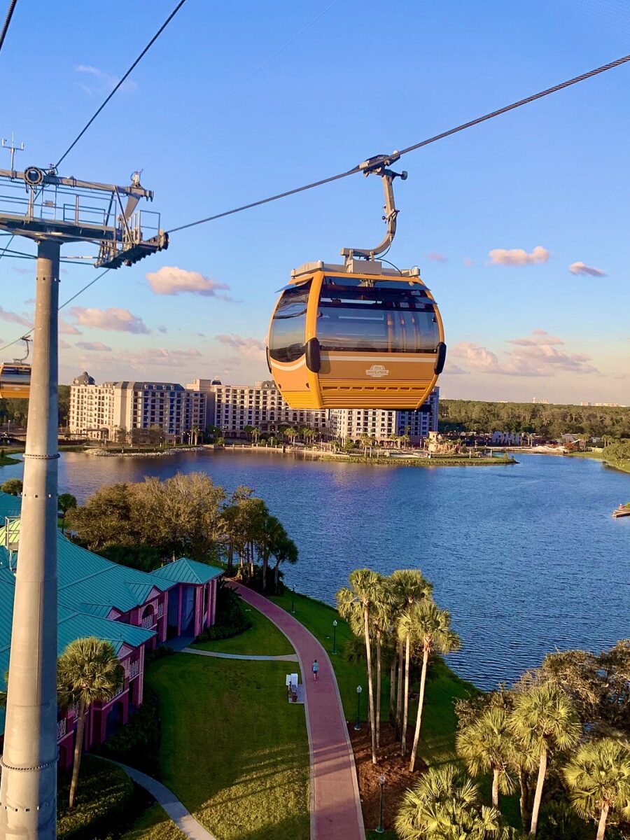 Disney Skyliner gondolas travelling on their cable above Disney's Caribbean Beach Resort, with a lake and resort buildings below