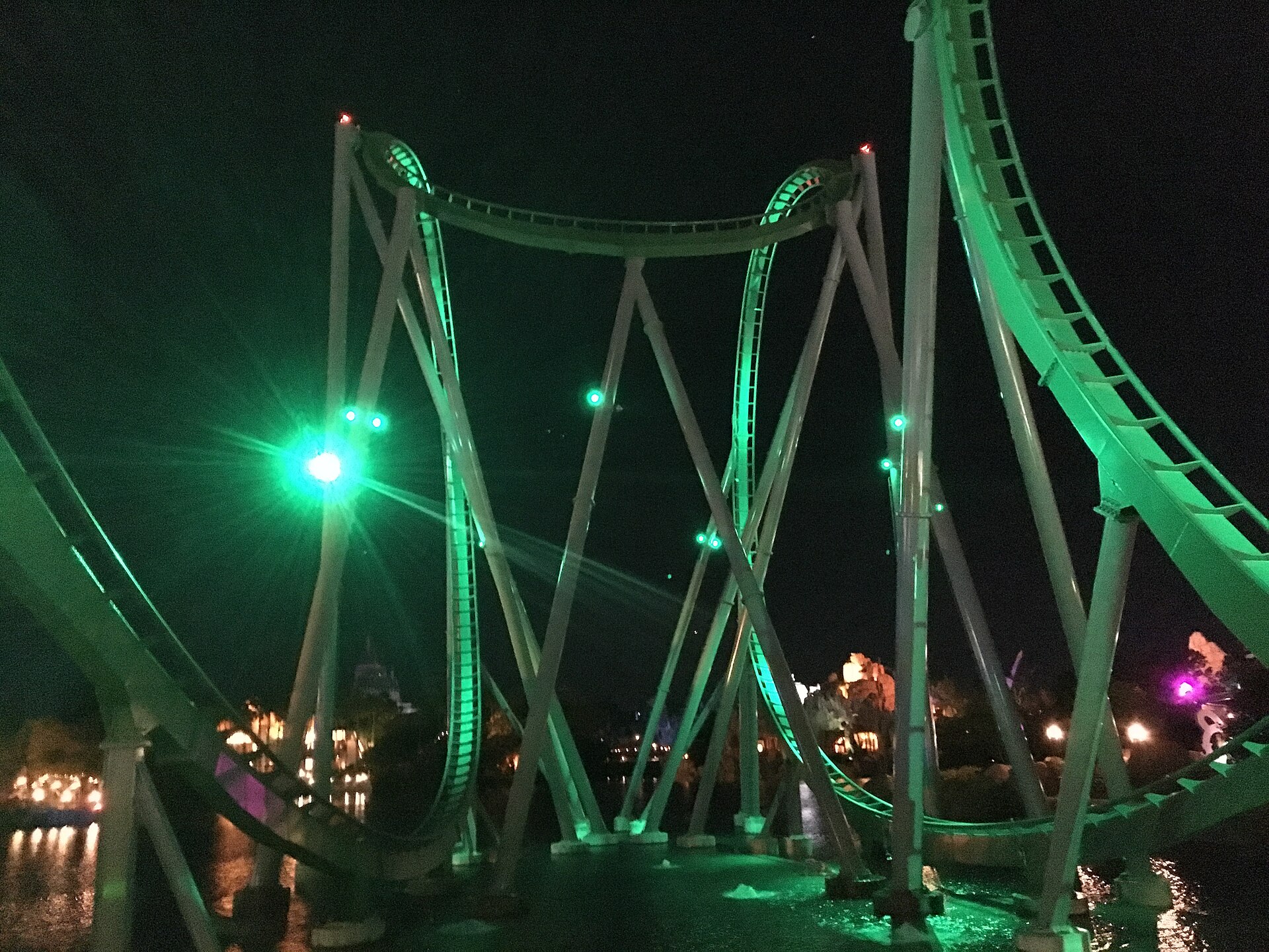 The Incredible Hulk Coaster's track and supports lit green at night over the lagoon at Islands of Adventure