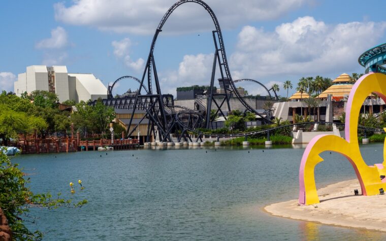 VelociCoaster's black top hat rising over the Islands of Adventure lagoon, with Jurassic Park's thatched buildings to the right and Seuss Landing's colorful arches in the foreground