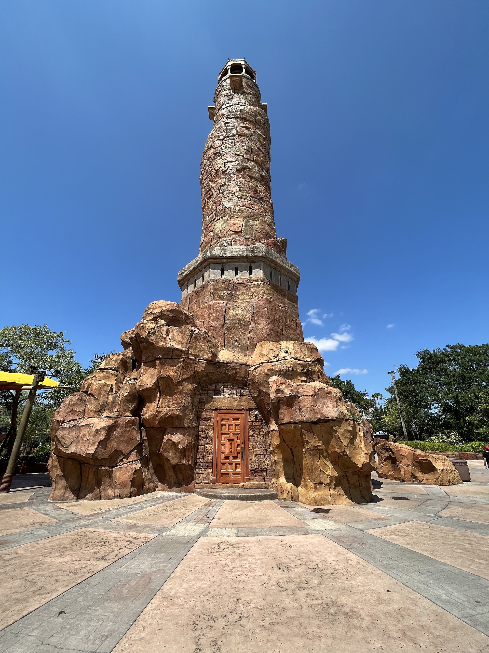 The tall stone Pharos lighthouse at the entrance to Islands of Adventure, rising above rockwork under a blue sky