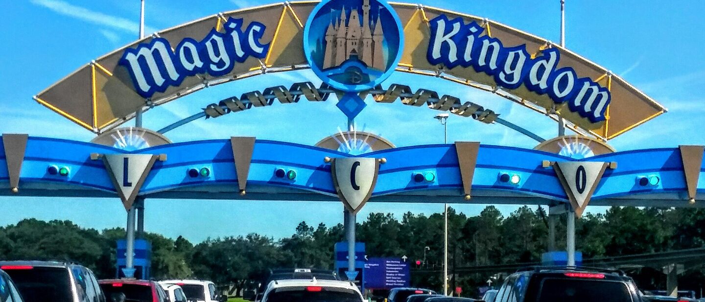 The blue and gold Magic Kingdom entrance arch over a line of cars waiting at the toll plaza on a sunny day