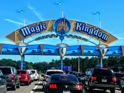 The blue and gold Magic Kingdom entrance arch over a line of cars waiting at the toll plaza on a sunny day