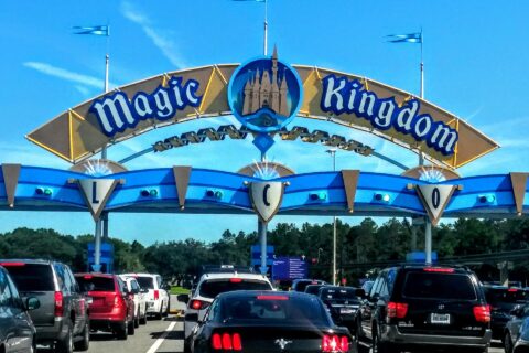 The blue and gold Magic Kingdom entrance arch over a line of cars waiting at the toll plaza on a sunny day