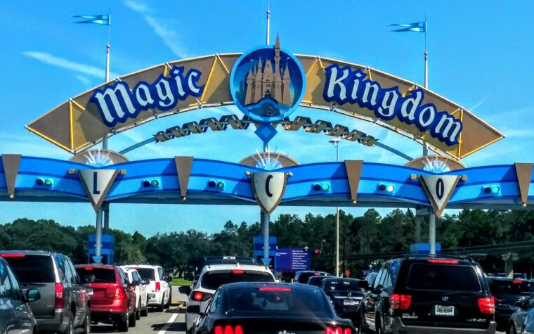 The blue and gold Magic Kingdom entrance arch over a line of cars waiting at the toll plaza on a sunny day