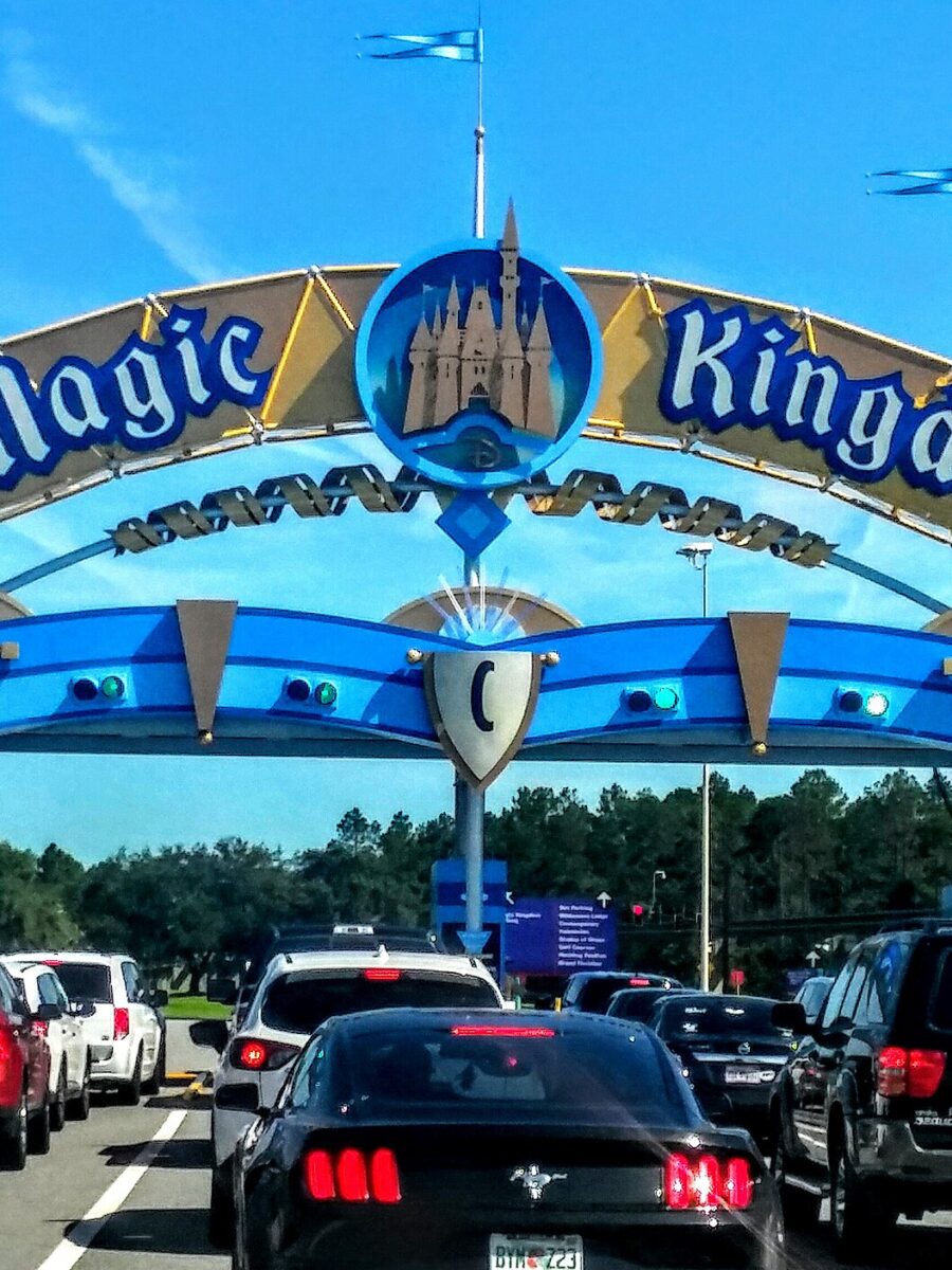 The blue and gold Magic Kingdom entrance arch over a line of cars waiting at the toll plaza on a sunny day