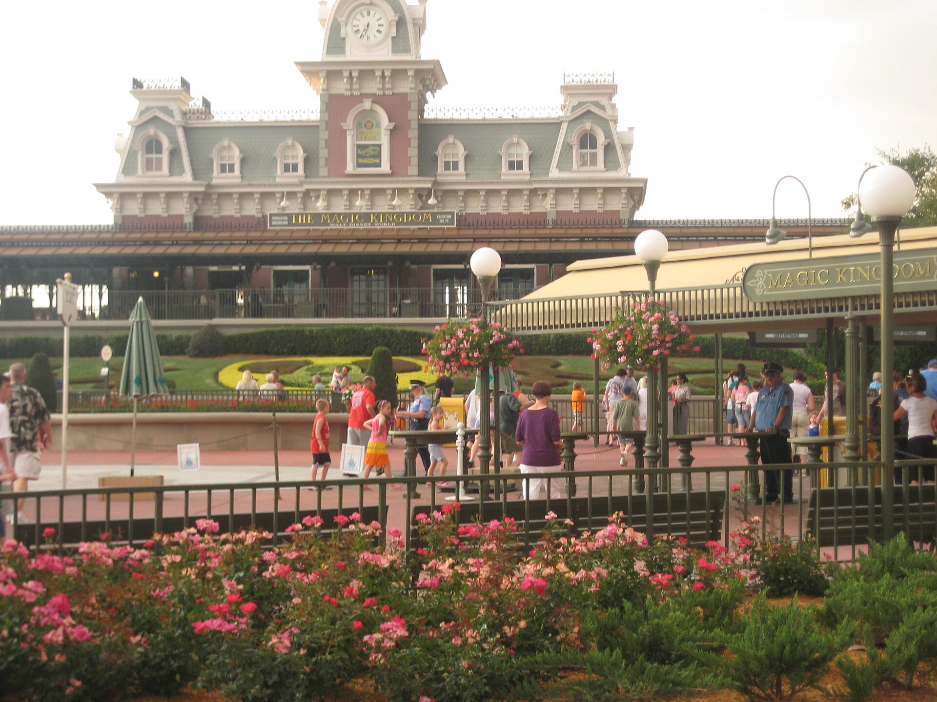 Guests in the entrance plaza below Magic Kingdom's Main Street railroad station, with flower beds in the foreground