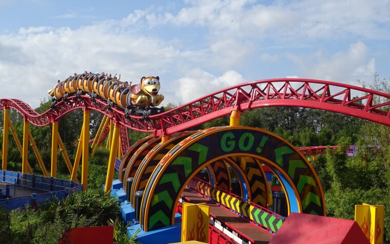 A Slinky Dog Dash train full of riders with raised arms on the red and yellow track in Toy Story Land at Hollywood Studios