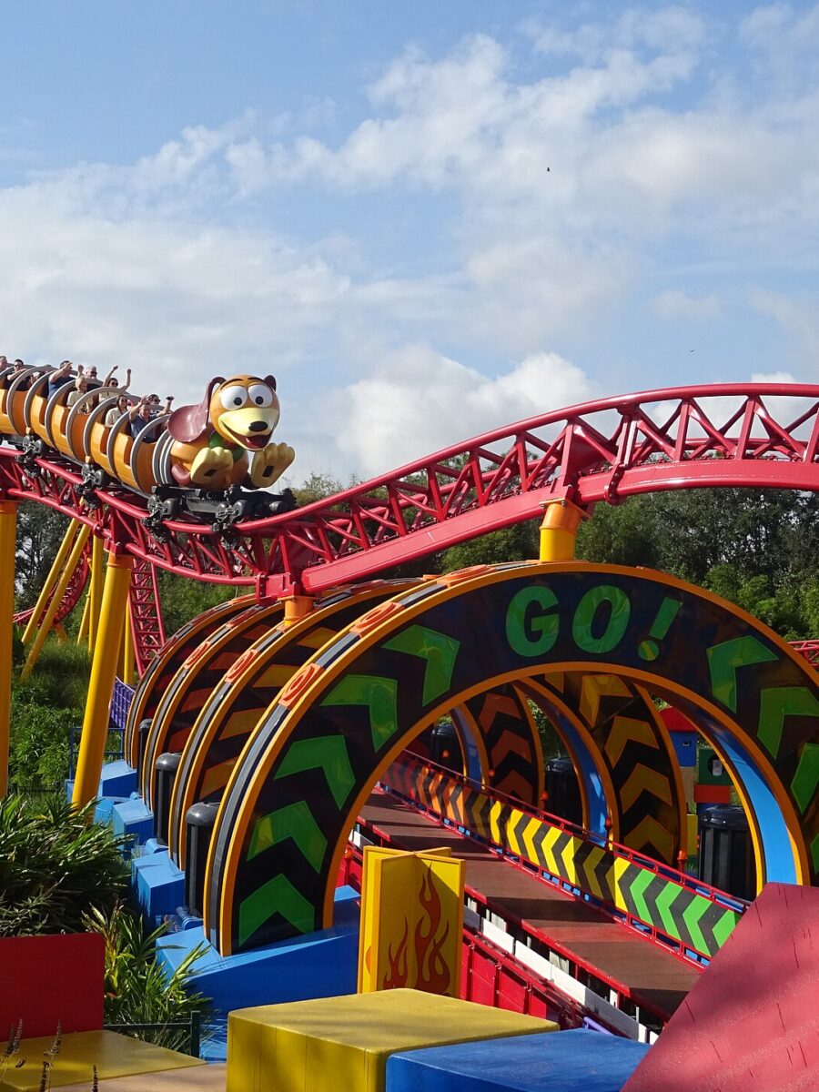 A Slinky Dog Dash train full of riders with raised arms on the red and yellow track in Toy Story Land at Hollywood Studios