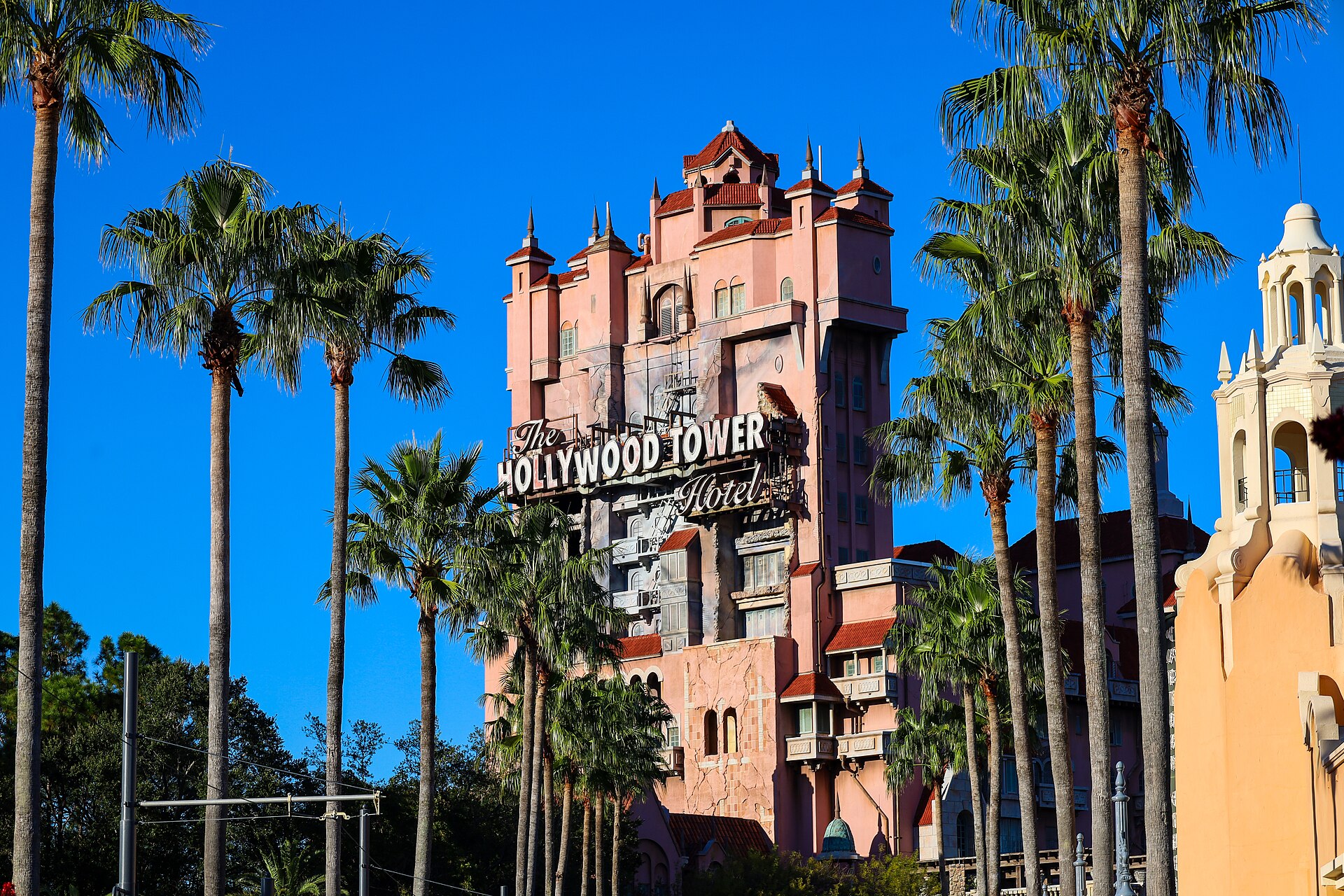 The Hollywood Tower Hotel facade of The Twilight Zone Tower of Terror rising behind tall palm trees under a clear blue sky