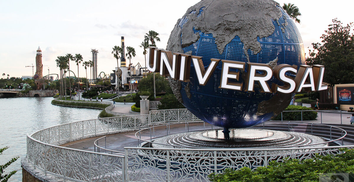 The large rotating Universal globe on its fountain plinth beside the lagoon at Universal Orlando, with palm trees and a lighthouse in the distance