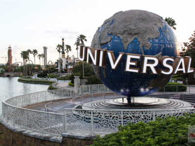 The large rotating Universal globe on its fountain plinth beside the lagoon at Universal Orlando, with palm trees and a lighthouse in the distance